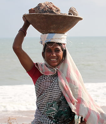 Smiling Indian woman carrying heavy rocks on her head at the beach