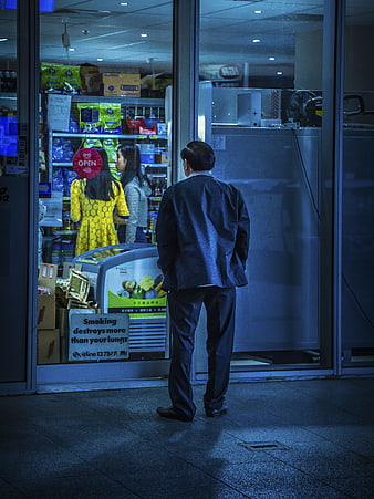 Man standing outside convenience store at night looking in