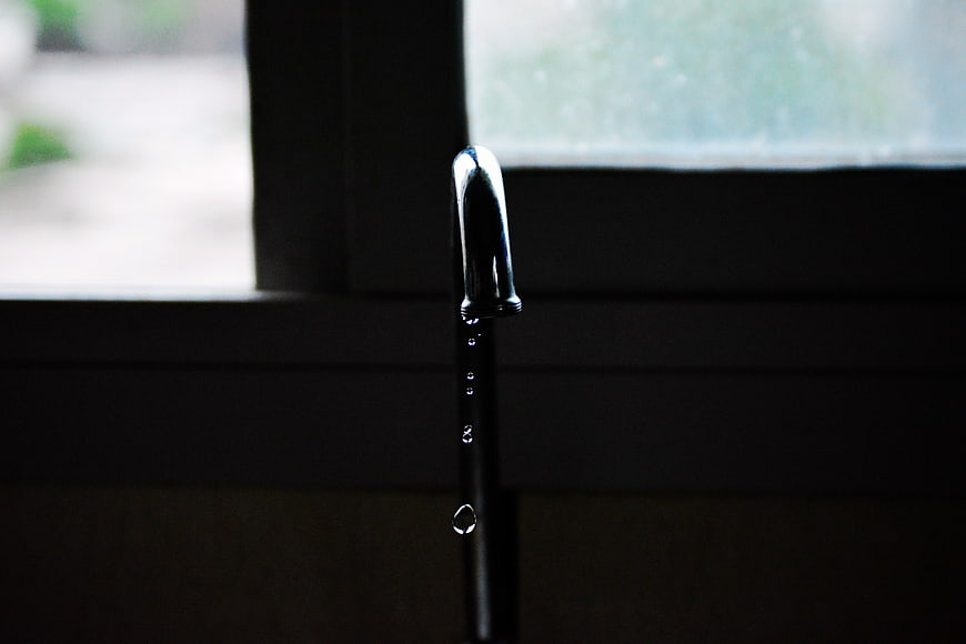 Dripping faucet with water drops against dark background