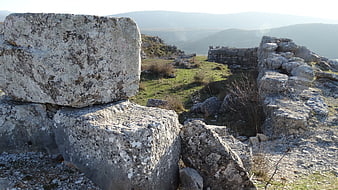 Ancient stone ruins on a grassy hilltop with mountain view