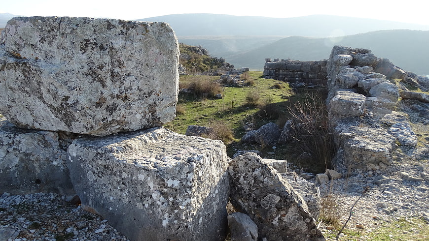 Ancient stone ruins on a grassy hilltop with mountain view