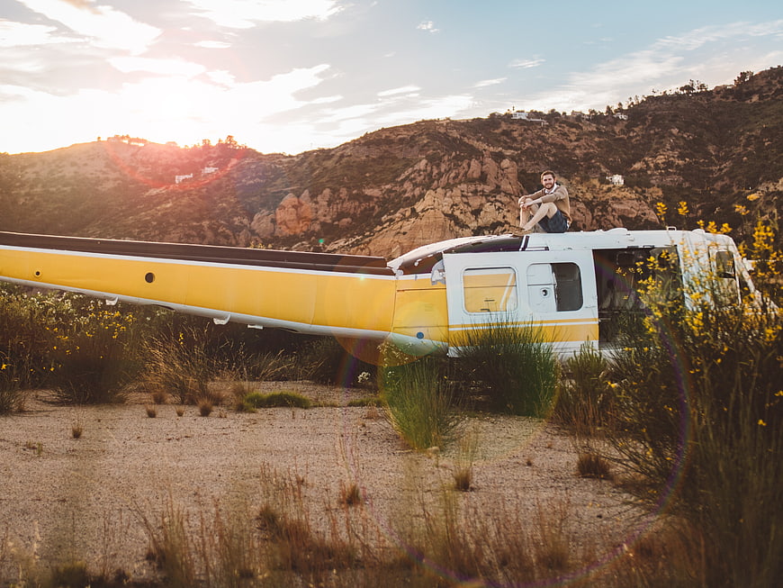 Man sitting on small airplane in desert landscape at sunset