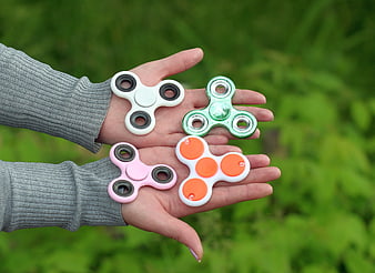 Hands holding four colorful fidget spinners against green background