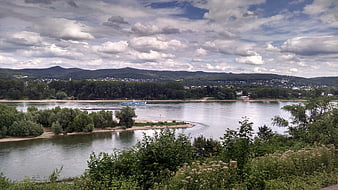 Wide river landscape with boats and distant hills under cloudy sky