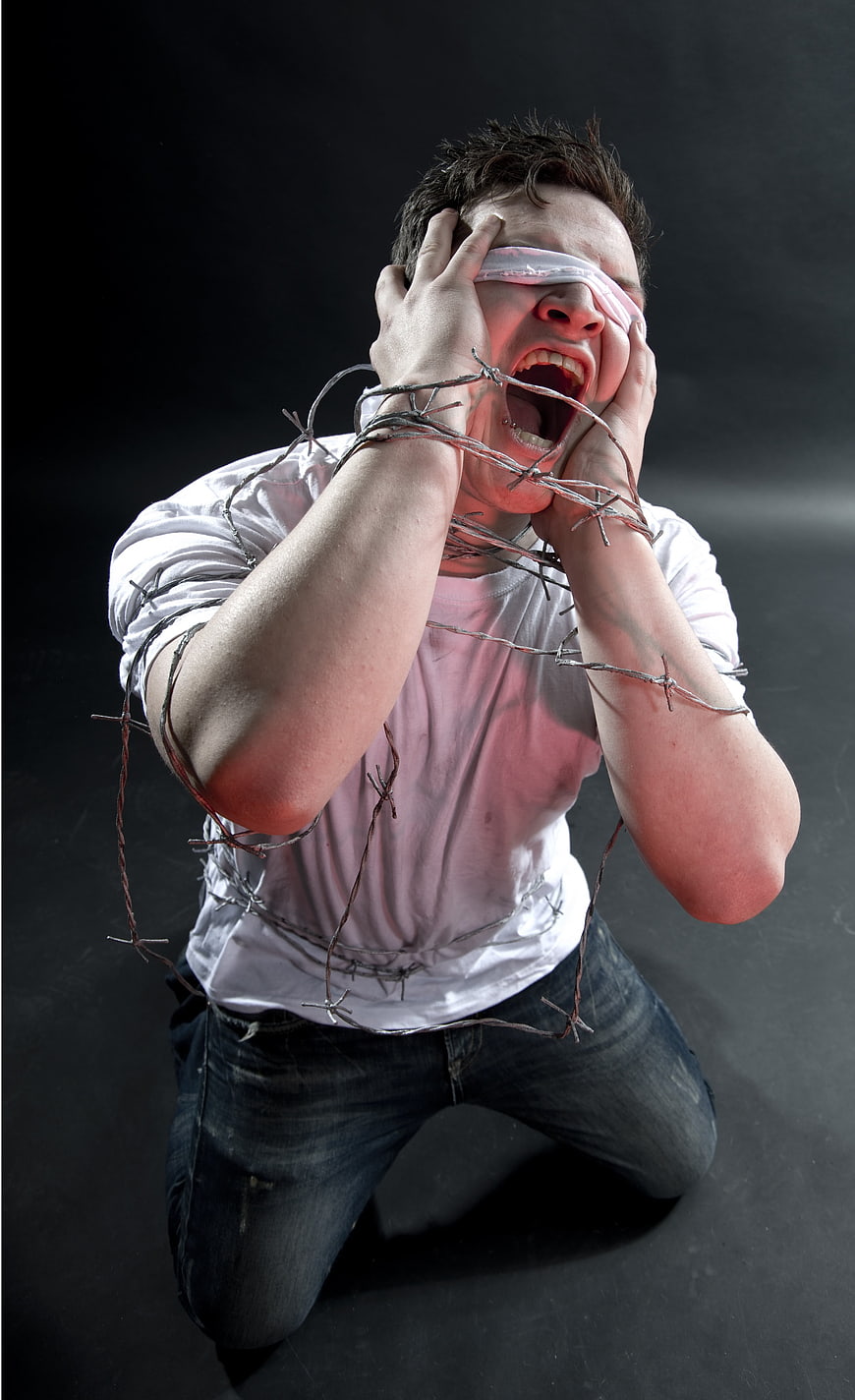 Blindfolded man screaming while bound by barbed wire