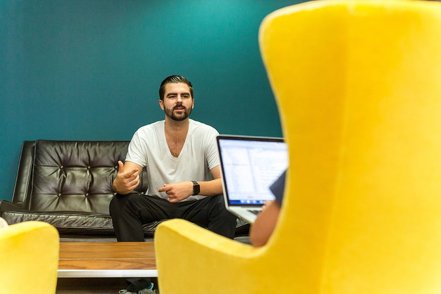 Man in white t-shirt talking in office with yellow chair