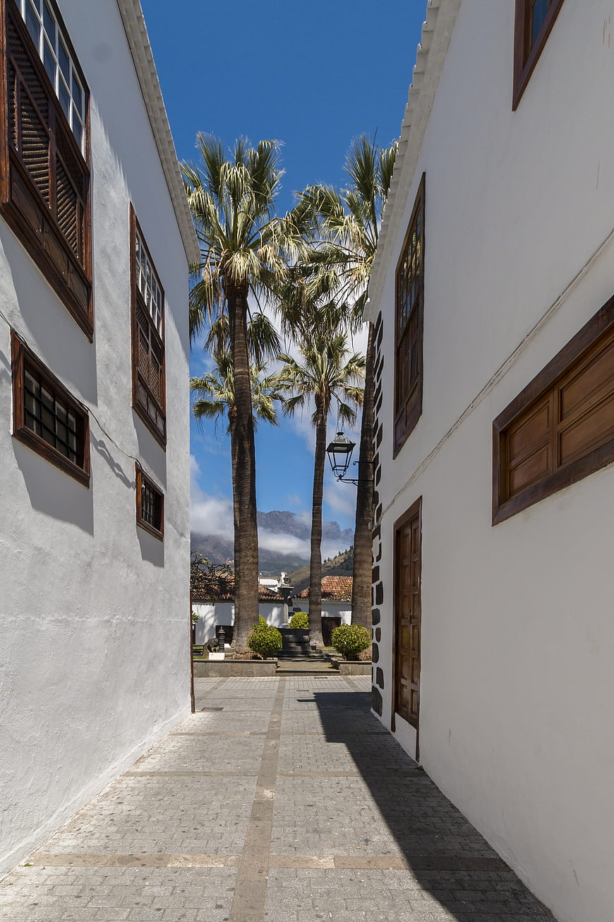 Narrow white alley with palm trees and mountains in background