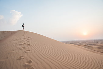 Lone Traveler Walking on Sand Dunes at Sunset