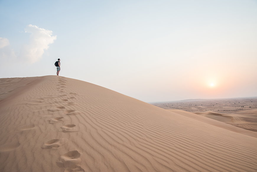 Lone Traveler Walking on Sand Dunes at Sunset
