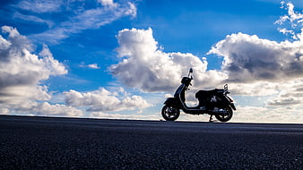 Silhouette of motor scooter on asphalt road under blue sky