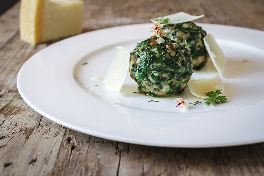 Spinach and cheese dumplings on a white plate with parmesan shavings