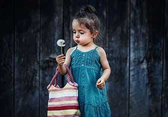 Little girl in teal dress holding dandelion and striped bag