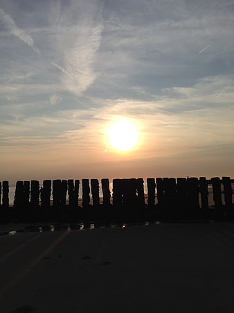 Silhouetted wooden groynes on beach at sunset