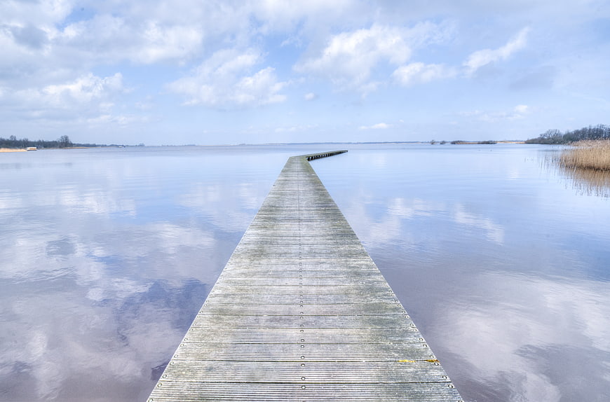 Serene wooden pier extending into calm blue water with sky reflections