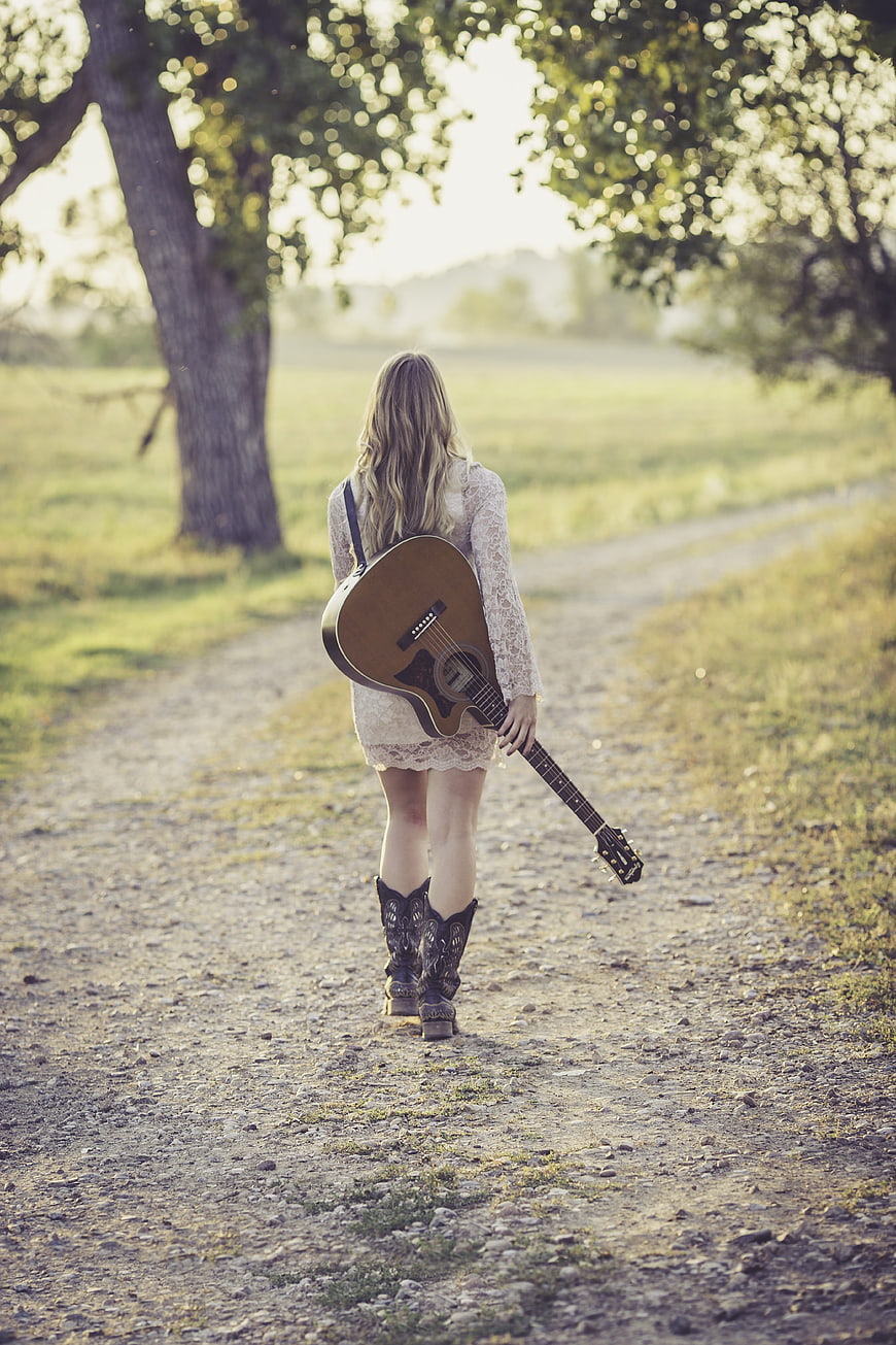 Woman with Guitar Walking on Country Road