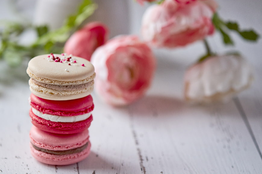 Stack of colorful macarons with pink flowers on white wood