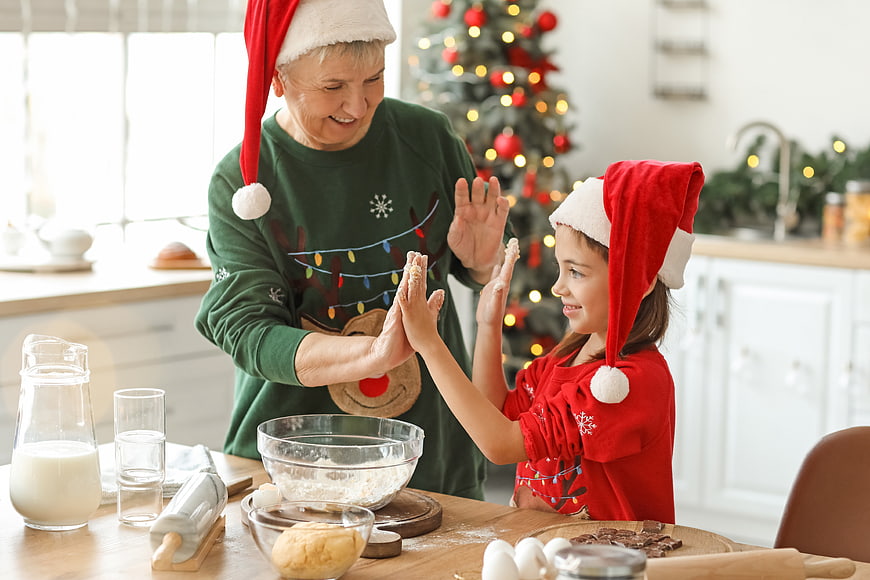 Grandmother and granddaughter baking cookies in kitchen with Christmas tree