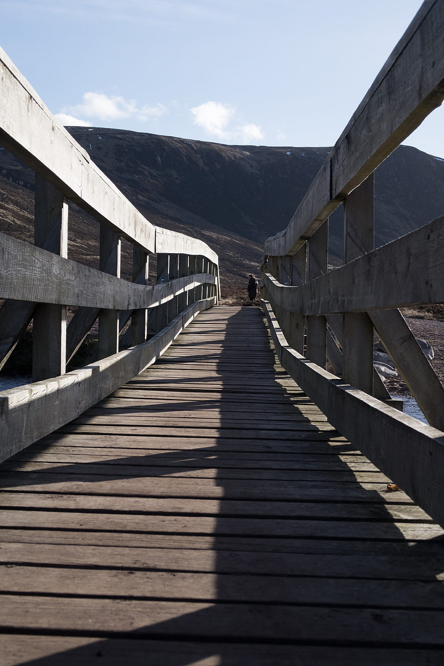 Wooden Bridge Leading to Mountain Landscape with Lone Walker