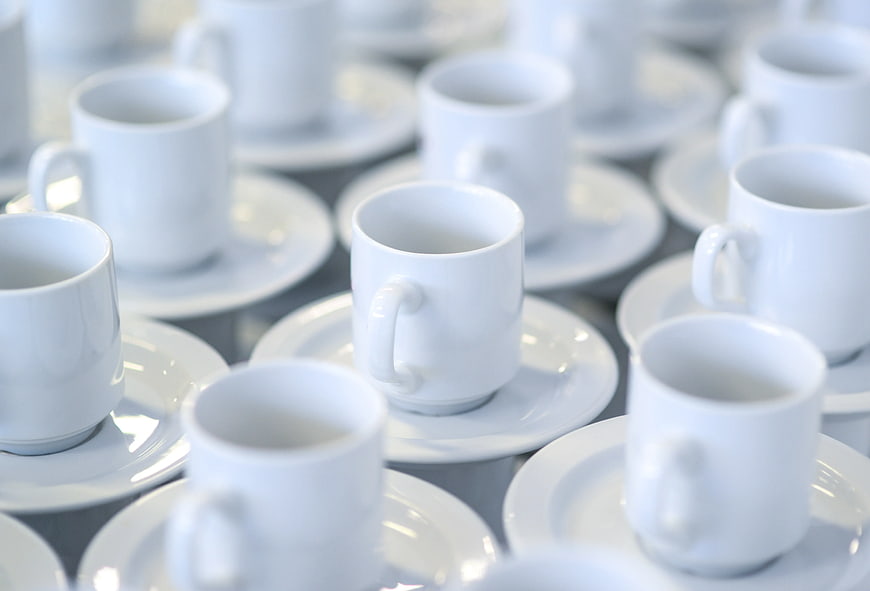 Rows of white ceramic coffee cups and saucers