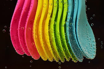 Colorful plastic spoons with water droplets on black background