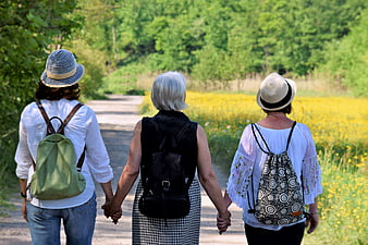 Three women holding hands walking on a country path