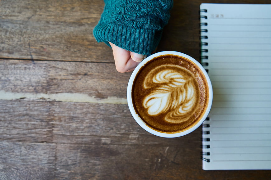Flat lay of latte art coffee cup with notebook on wooden table