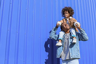 Happy father carrying child on shoulders against blue wall