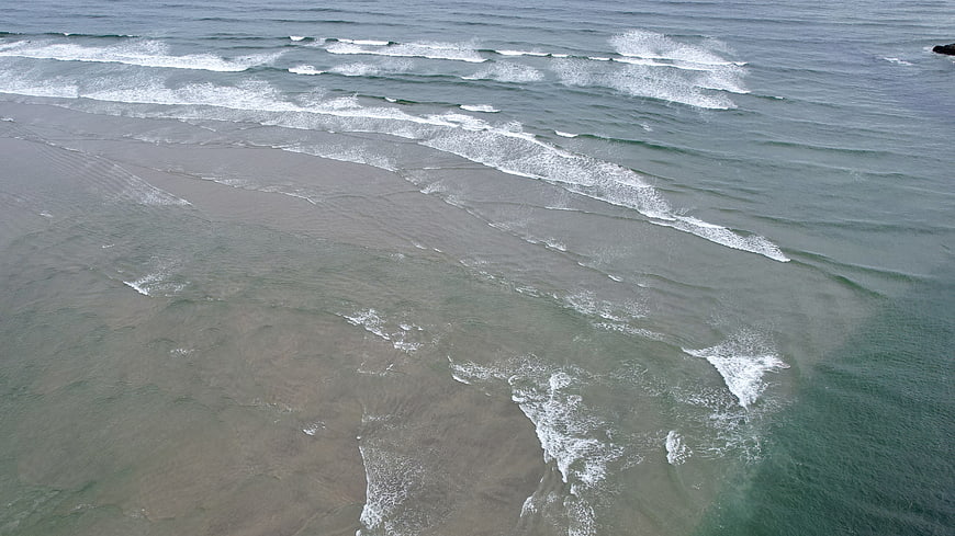 Aerial view of ocean waves rolling onto a sandy beach