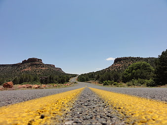 Low angle view of yellow road lines leading to red rock mountains