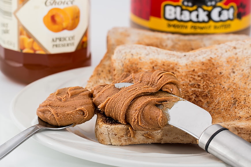 Spreading creamy peanut butter on whole wheat toast with jam