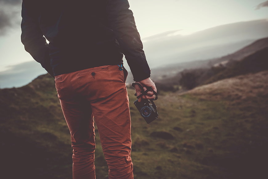 Man holding camera on mountain ridge overlooking valley