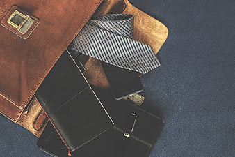 Flat lay of men's leather bag, necktie, notebook, and smartphone