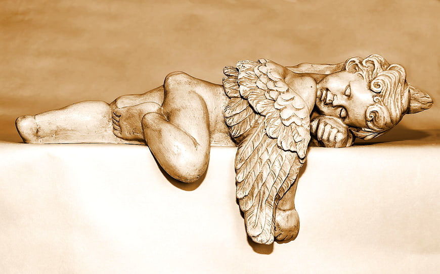 Sepia-toned sleeping cherub statue lying on ledge