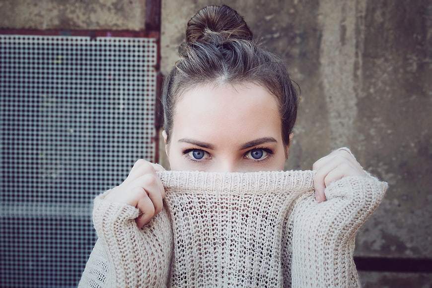 Woman with blue eyes peeking over beige knit sweater