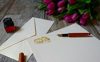 Wedding rings, fountain pen, and pink tulips on rustic wooden table