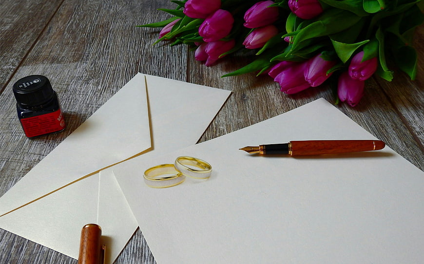 Wedding rings, fountain pen, and pink tulips on rustic wooden table