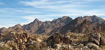 Rugged desert mountain range with rocky foreground and blue sky