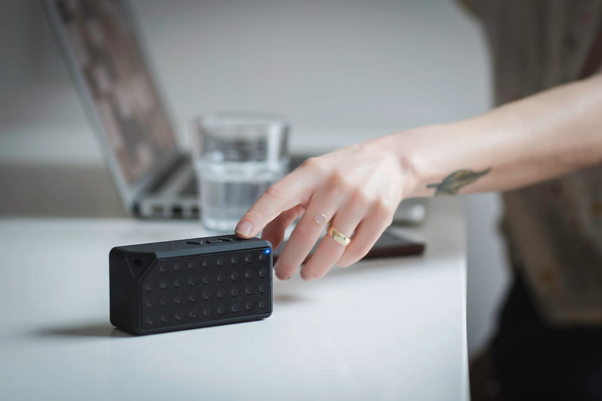 Hand pressing button on portable black speaker