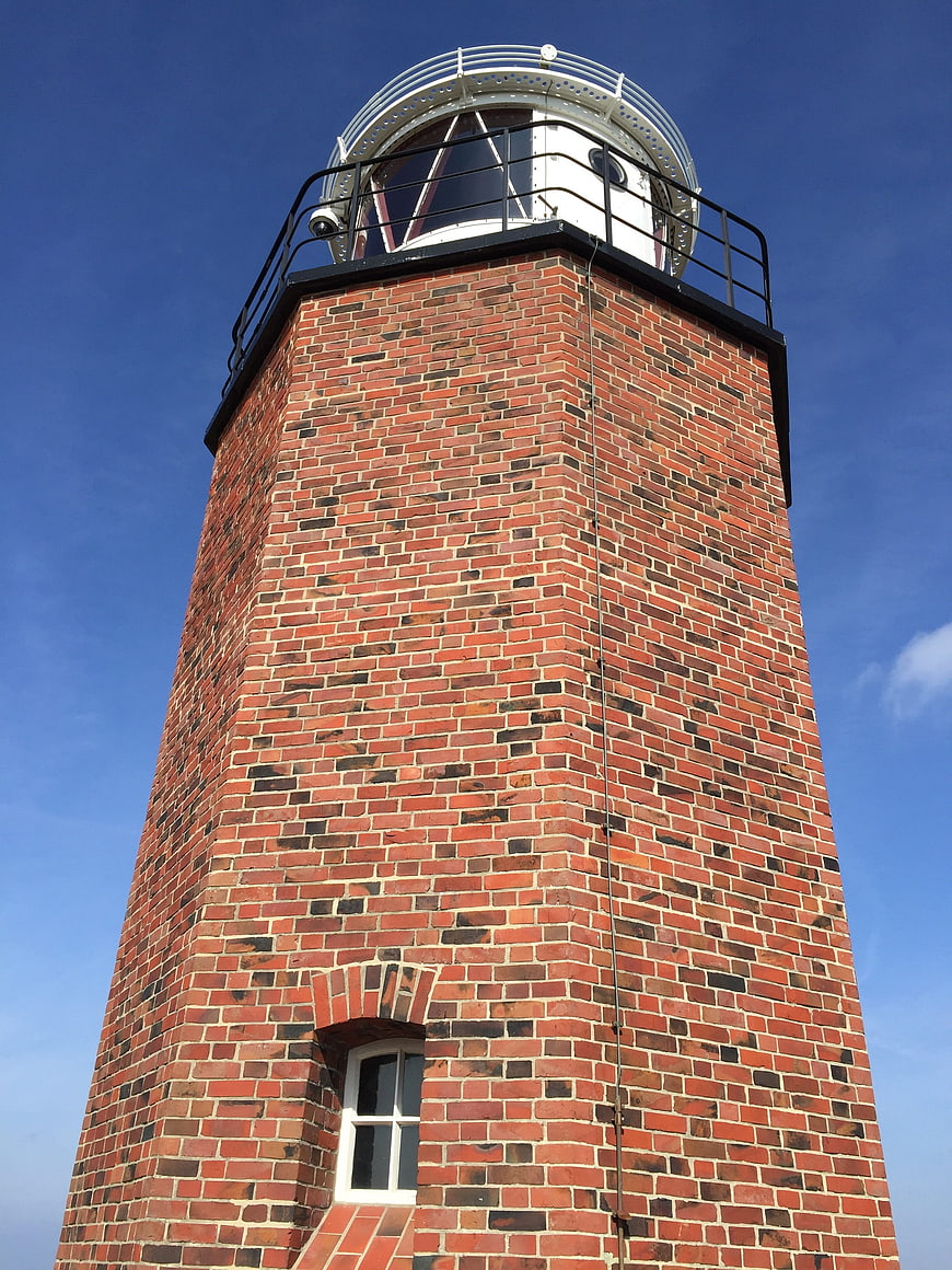Low angle view of red brick lighthouse against blue sky