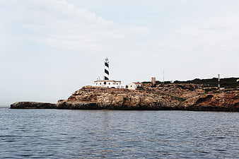 Black and white striped lighthouse on rocky coastal cliff