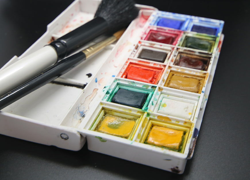 Used watercolor palette with paintbrushes on dark background