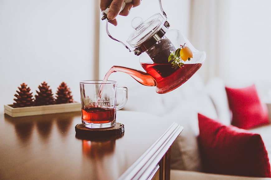 Pouring red herbal tea from glass teapot into mug