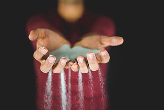 Hands pouring white sand against dark background
