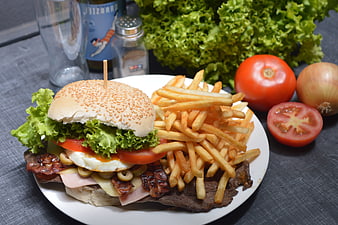 Delicious burger with fries, fresh vegetables, and condiments on a plate