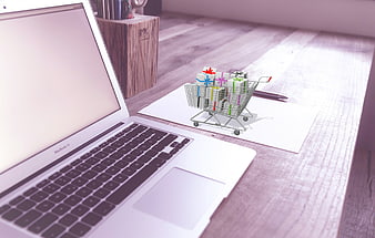 Miniature shopping cart with gifts on desk next to laptop