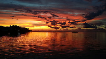 Dramatic Red Sunset Over Calm Water With Silhouetted Stilt Houses