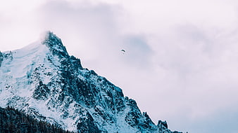 Paraglider soaring over snowy mountain peak in winter