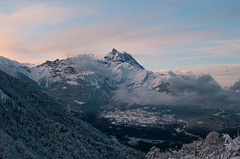Snowy Mountain Peak at Sunset with Clouds and Forest