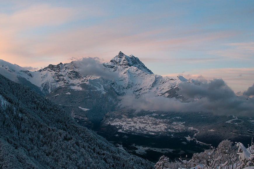 Snowy Mountain Peak at Sunset with Clouds and Forest