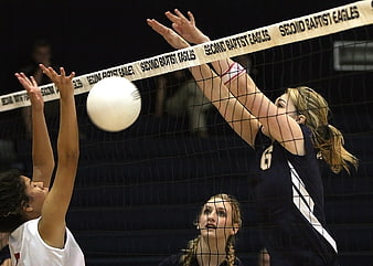 Female volleyball players blocking at the net during a match